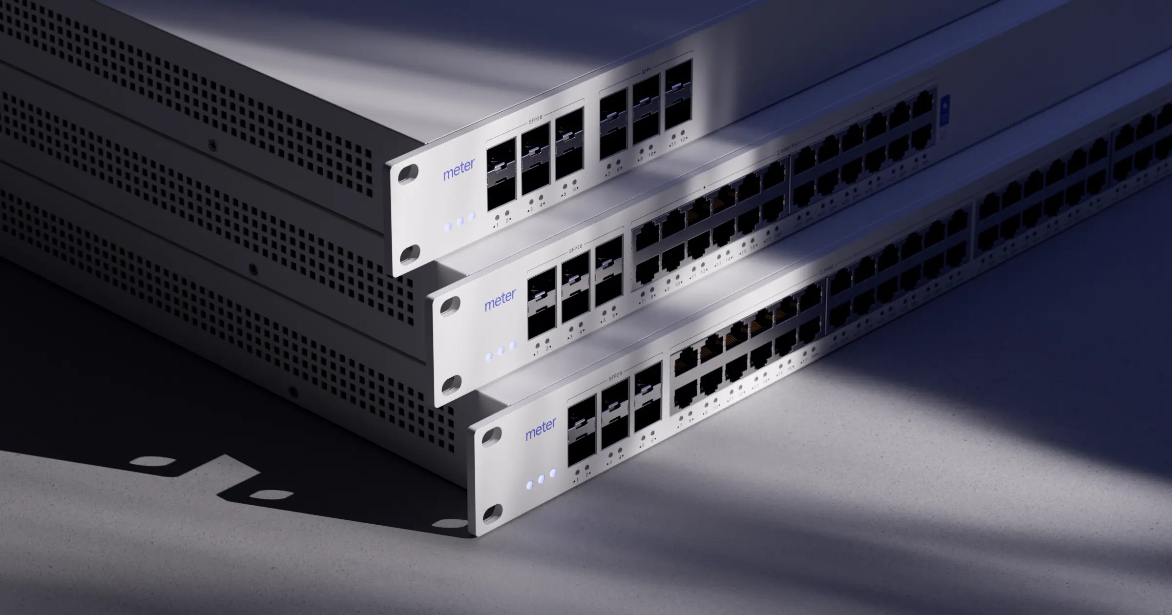 Three white Meter network switches stacked against a dark backdrop