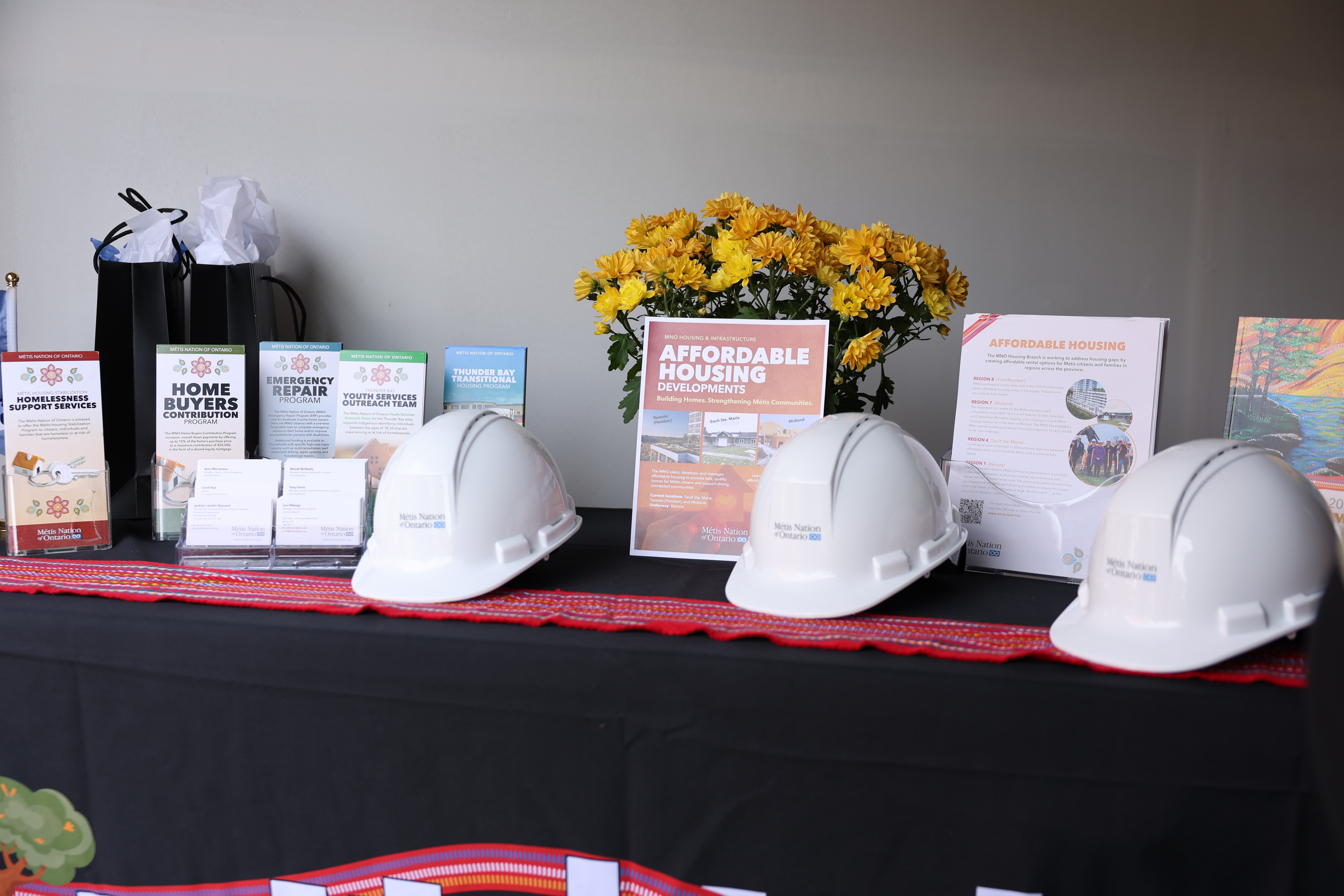MNO hard hats and housing-program brochures displayed on a Métis sash at the Midland opening
