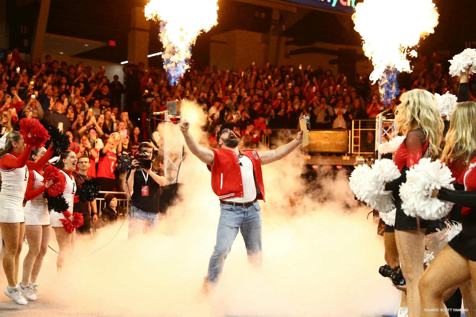 A sports entertainer making a dramatic entrance between cheerleaders and bursts of flame