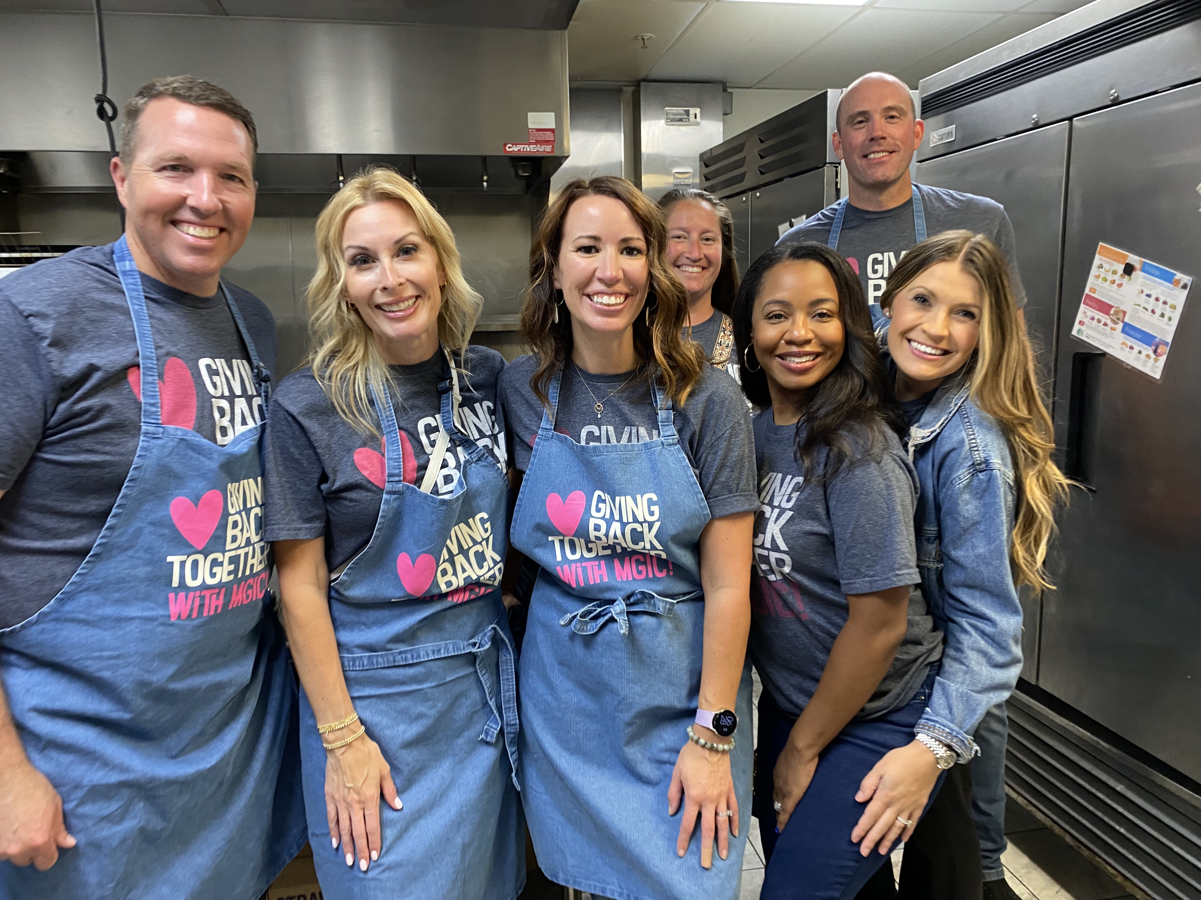 MGIC volunteers wearing Giving Back Together shirts and aprons in a kitchen