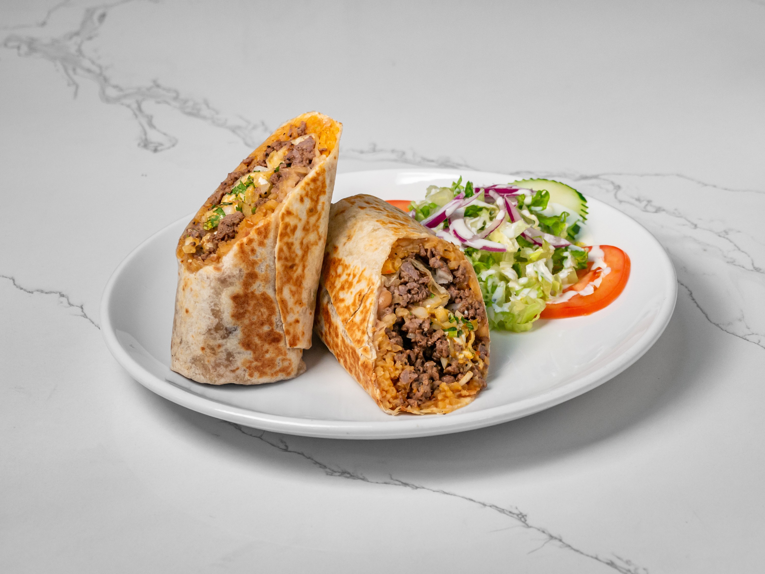 A cut burrito served with vegetables on a white plate