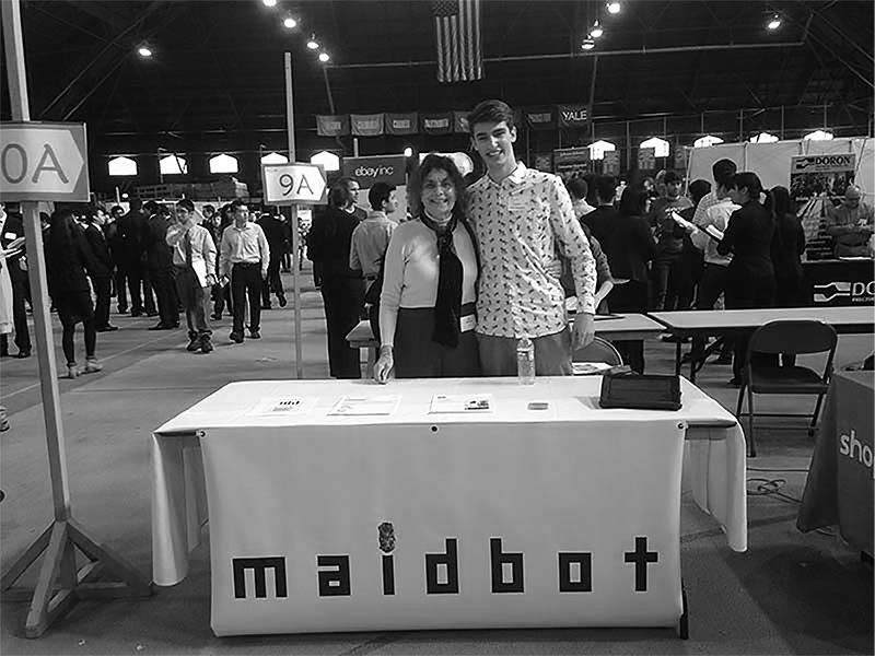 Micah Estis Green standing behind an early Maidbot booth at a career fair