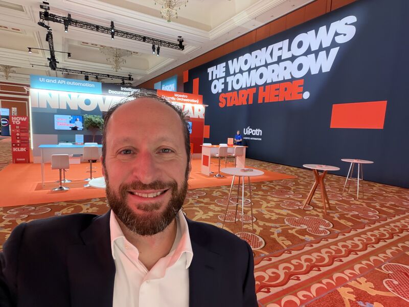 Michael Atalla at the UiPath Fusion conference, with an exhibition wall reading The workflows of tomorrow start here