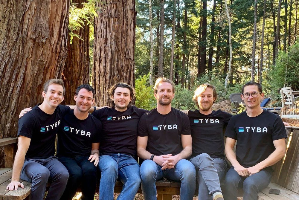 Michael Baker, third from left, seated with five Tyba colleagues beneath redwood trees
