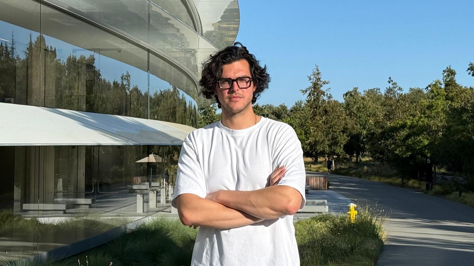 Michael Belhassen standing outside Apple Park, beside its curved glass exterior
