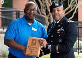Michael Bender and Major Whitted holding a partnership plaque at an Eyemart Express Army hiring ceremony