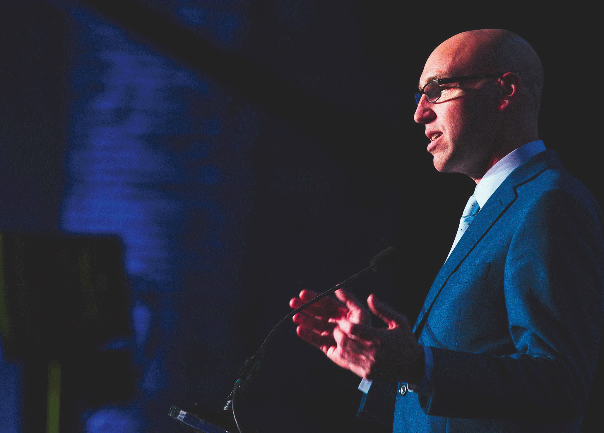Michael Bourque speaking at a lectern in a blue suit