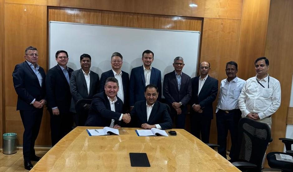 Michael Briggs and Shenu Agarwal shake hands over signed agreements, with Nidec and Ashok Leyland colleagues behind them.