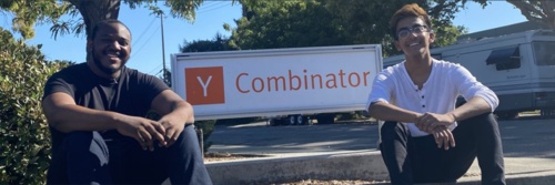 Michael Broughton and Ayush Jain sitting beside a Y Combinator sign