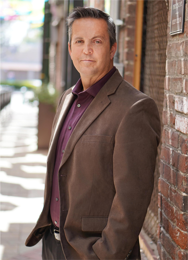 Michael Caldwell standing beside a brick wall in a brown jacket