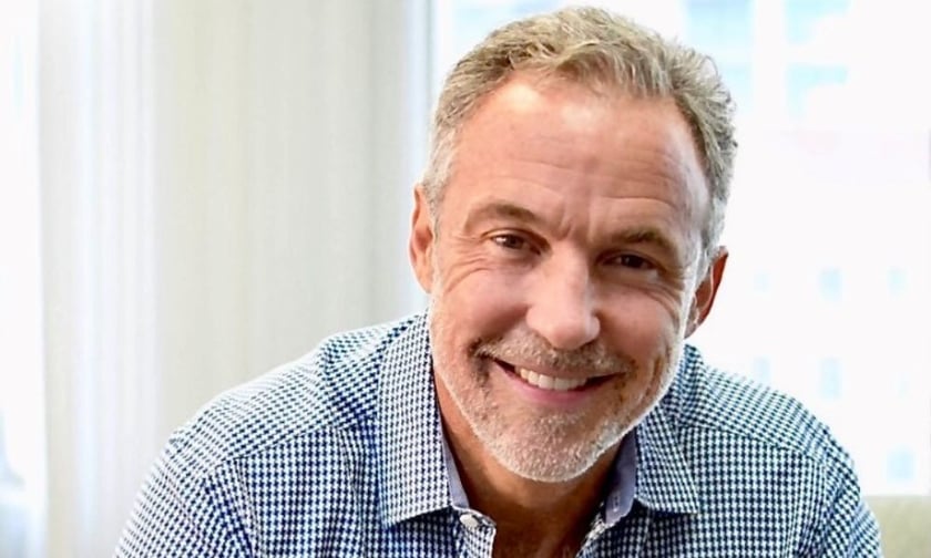 Michael Carricarte smiling in a checked shirt during a press portrait