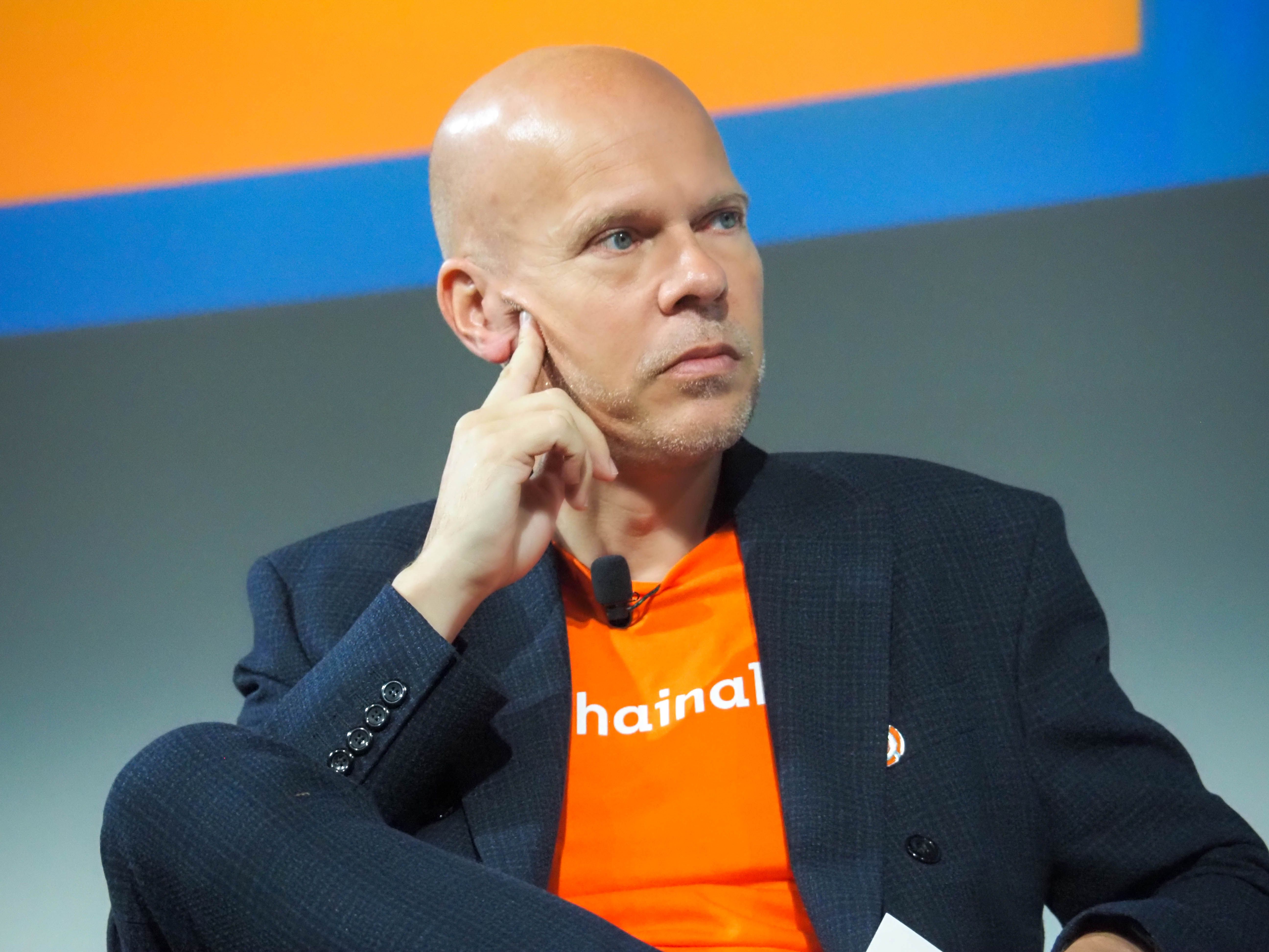Michael Gronager seated at a conference, wearing an orange Chainalysis T-shirt under a dark jacket