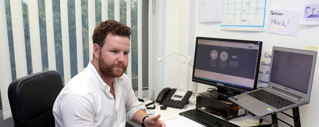 Michael Grupp at his desk in the Thesius office, with a monitor, laptop and handwritten notes
