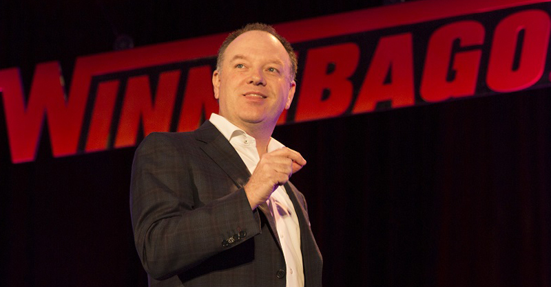 Michael Happe speaking onstage in front of illuminated Winnebago lettering