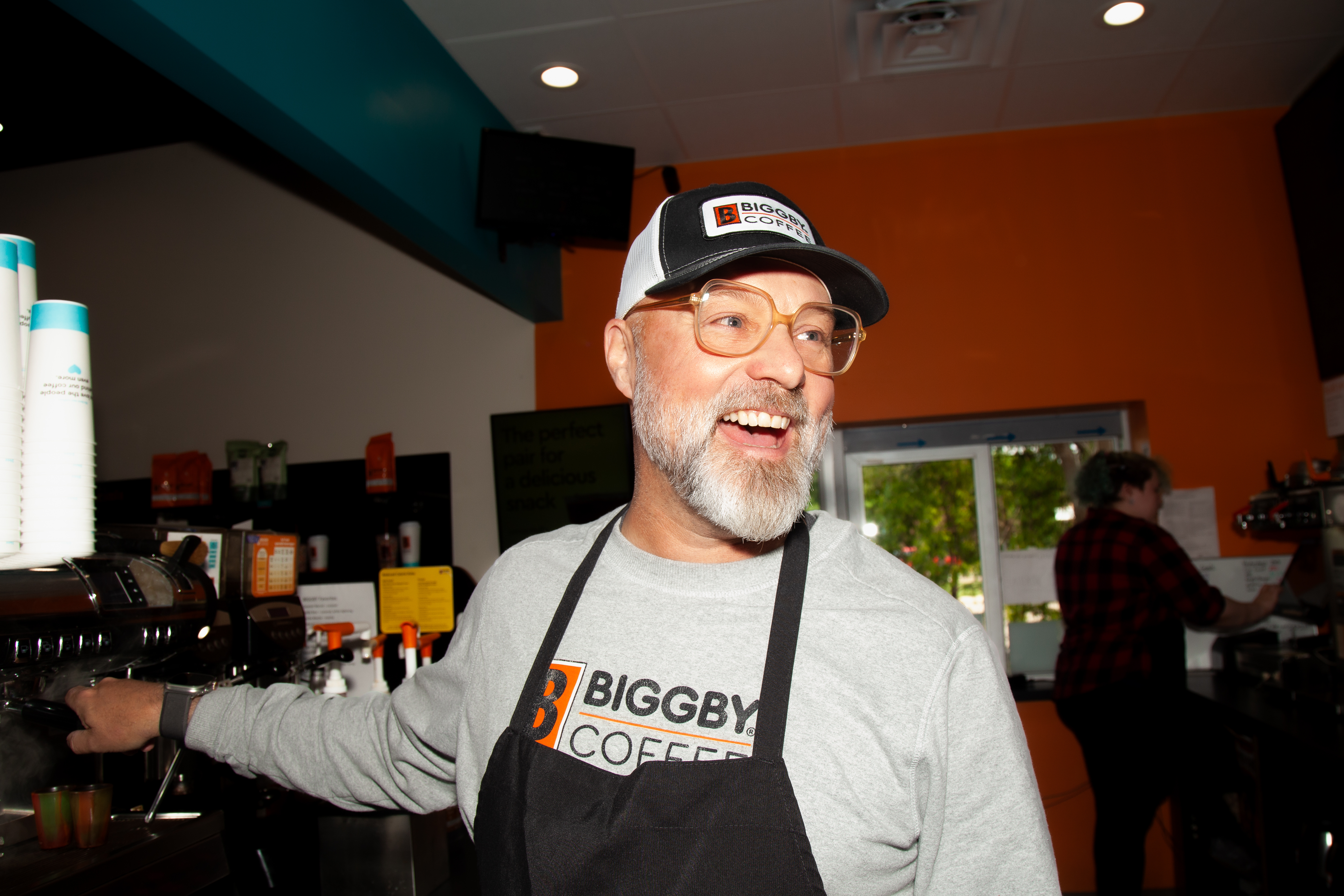 Michael McFall wearing a BIGGBY apron and cap behind a café counter