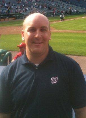 Michael Letschin smiling beside a baseball field in a Washington Nationals shirt