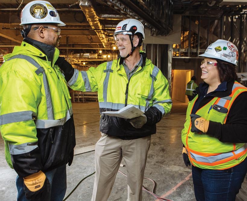 Michael McKelvy, center, wearing a hard hat and high-visibility jacket while talking with two colleagues inside a construction project