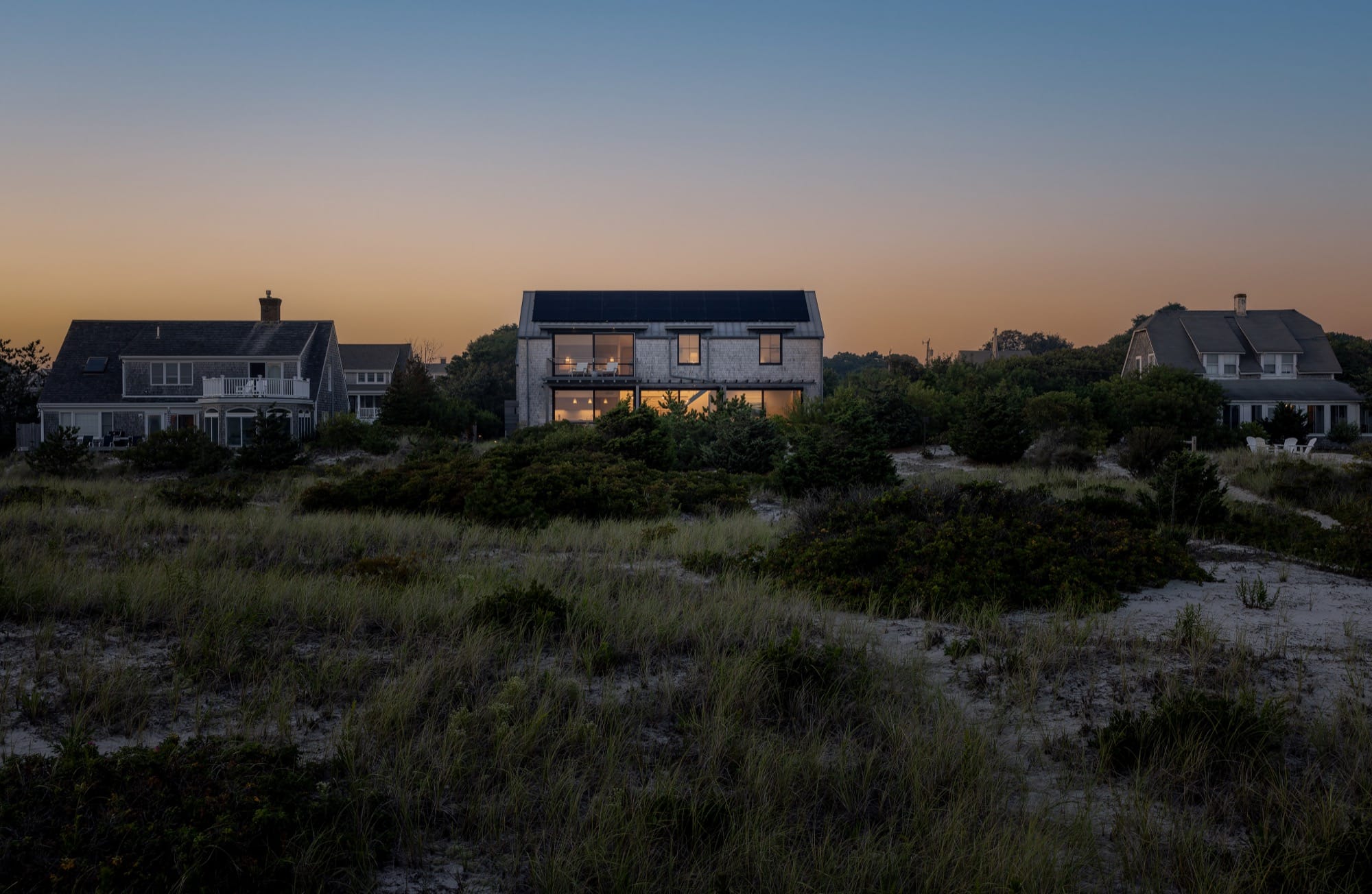 Cape Cod Hemp House with rooftop solar panels, seen among neighboring coastal houses at dusk
