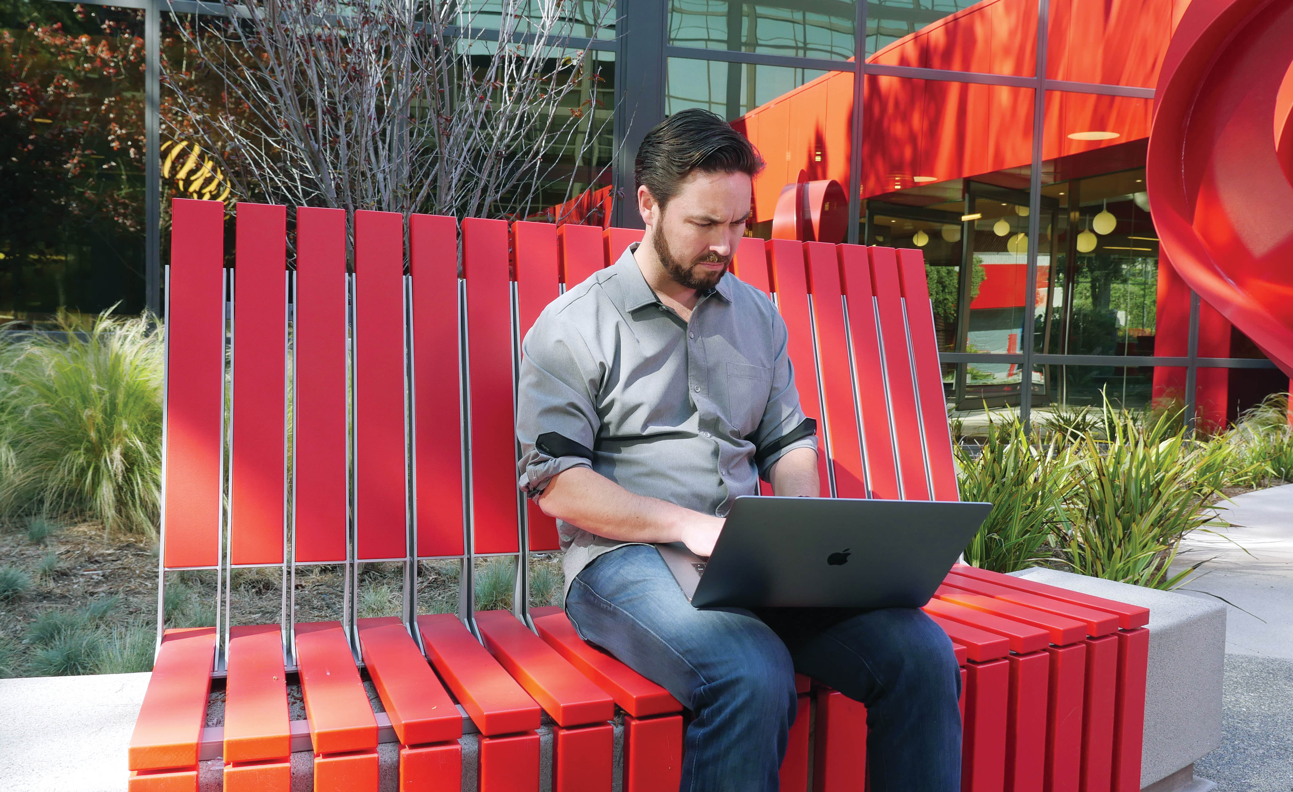 Michael Mothner working on a laptop while seated on a bright red outdoor bench