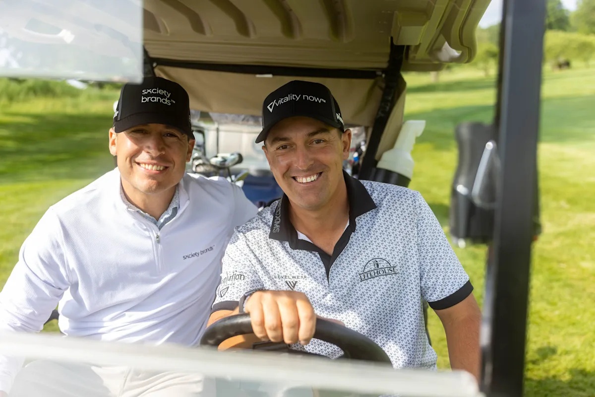 Michael Sirpilla, left, and golfer Justin Lower smiling in a golf cart