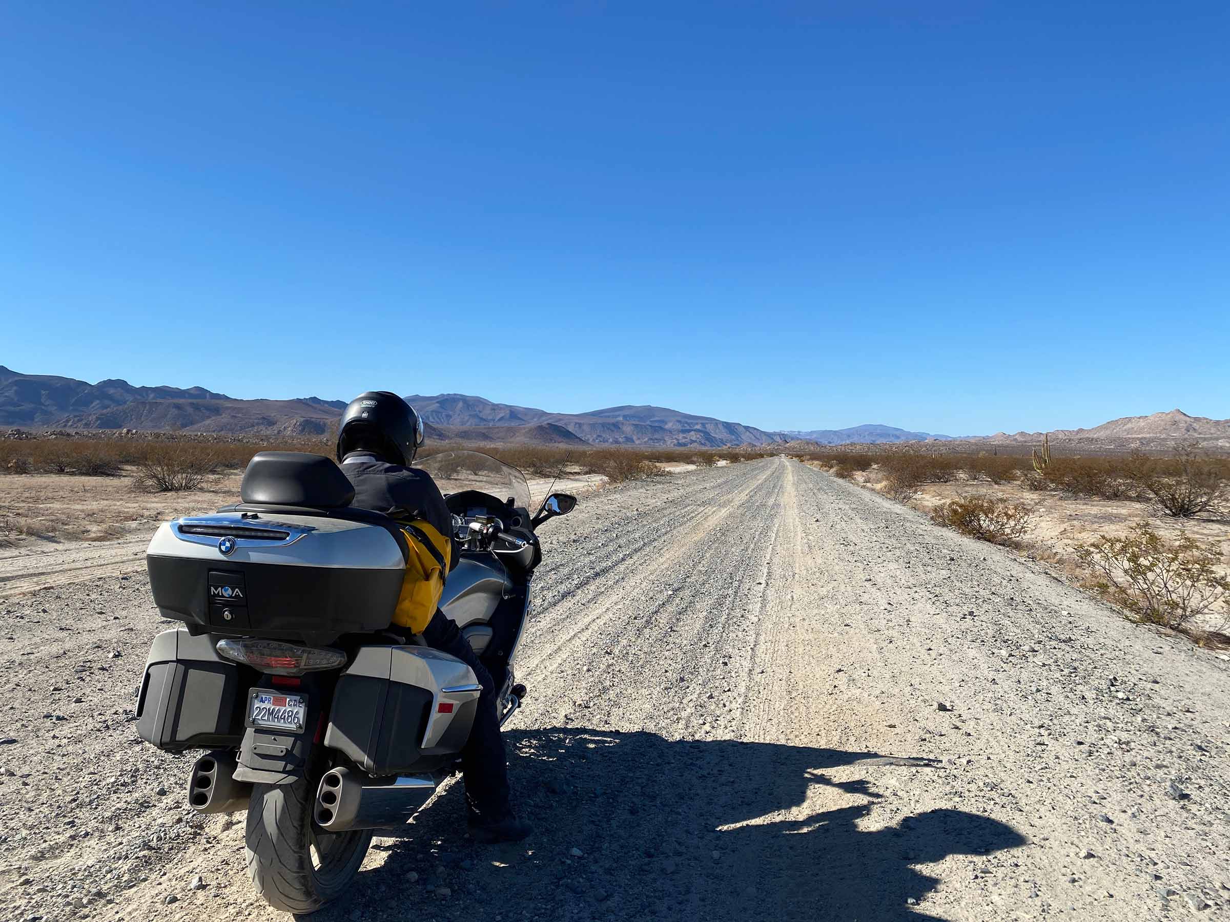 Michael Yang seated on his motorcycle facing a long gravel road through an open landscape