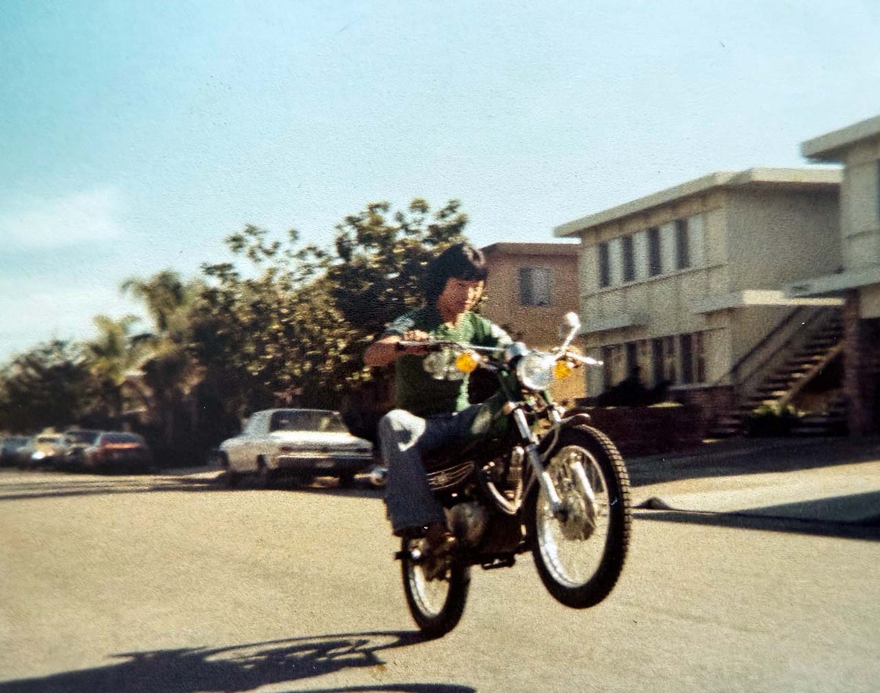 A young Michael Yang riding a Yamaha motorcycle with its front wheel raised