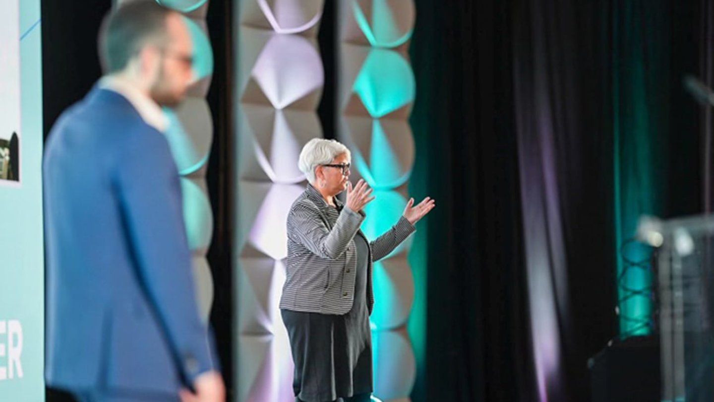 Michele Salomon speaking on stage at P2PI Live in Chicago while Gabriel Rozenwasser stands in the foreground