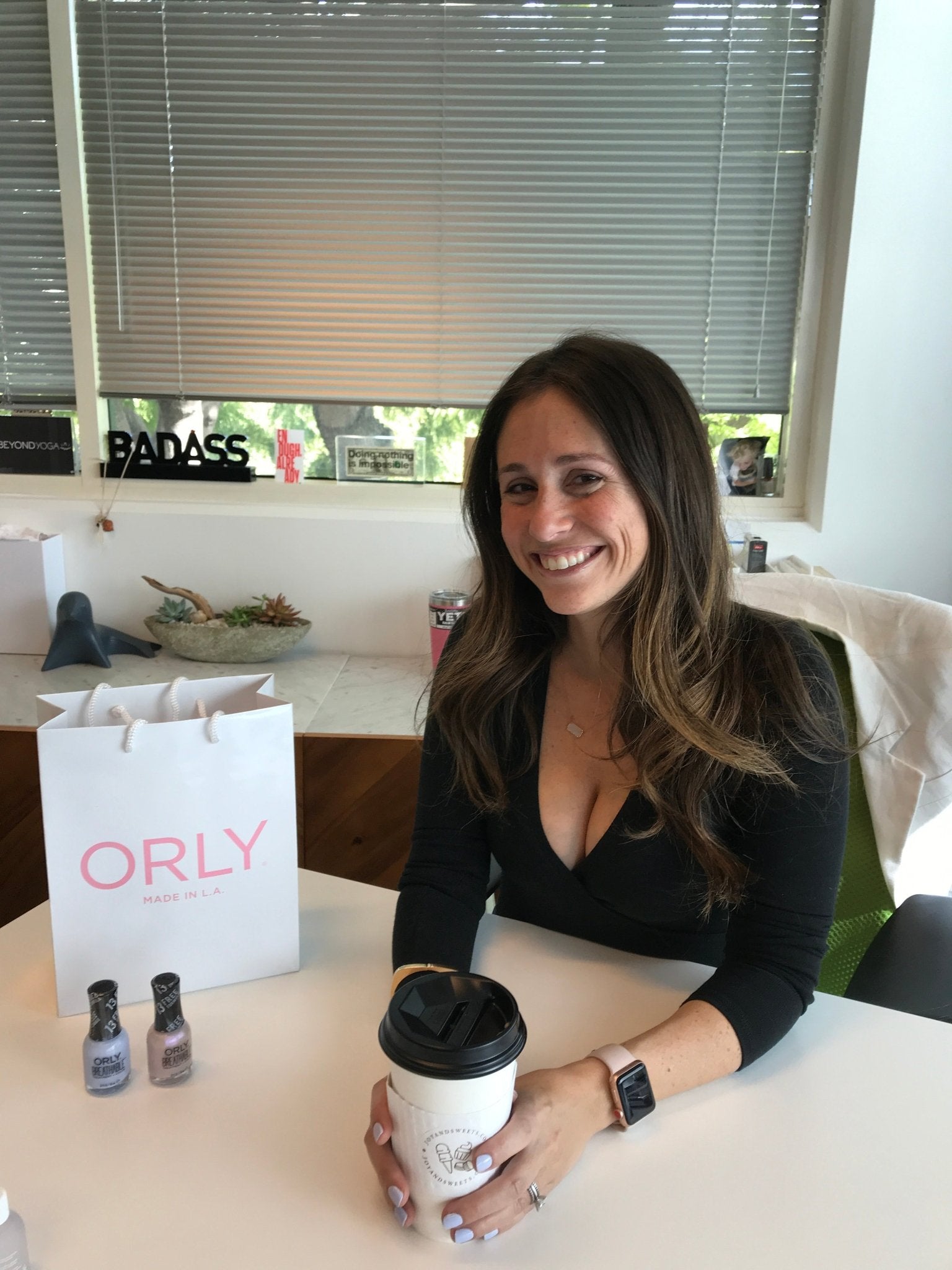 Michelle Wahler smiling at a desk with a coffee cup, nail polish and an ORLY bag
