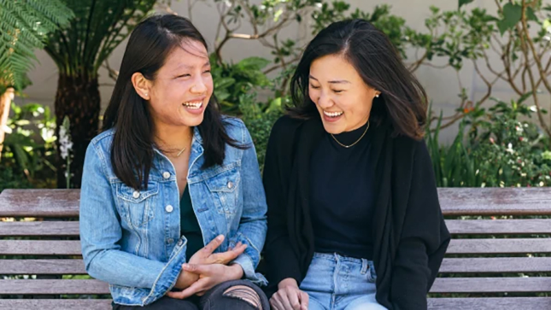 Tammy Hsu, left, and Michelle Zhu, right, laughing together on a garden bench