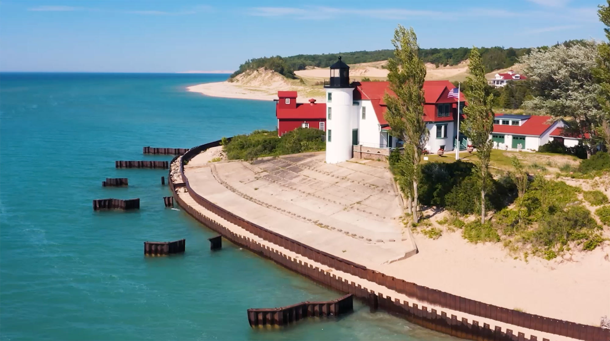A red-roofed Michigan lighthouse beside blue water and sand dunes