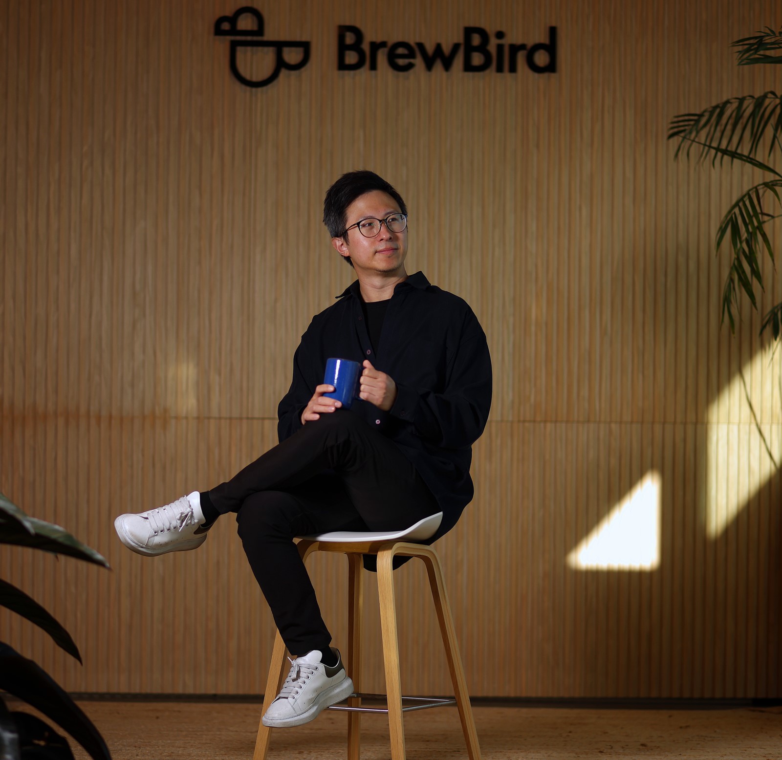 Mickey Du sits with a cup of coffee beneath the BrewBird sign in the company's San Carlos office