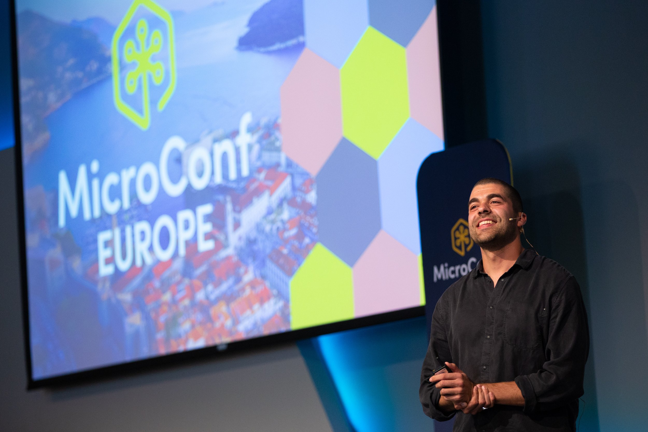 A speaker onstage at MicroConf Europe in front of a colorful conference screen