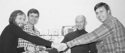 Early Micron team members join hands around a workbench
