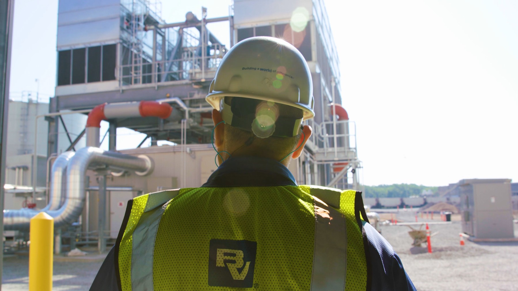 A worker in a Black & Veatch hard hat overlooking industrial equipment