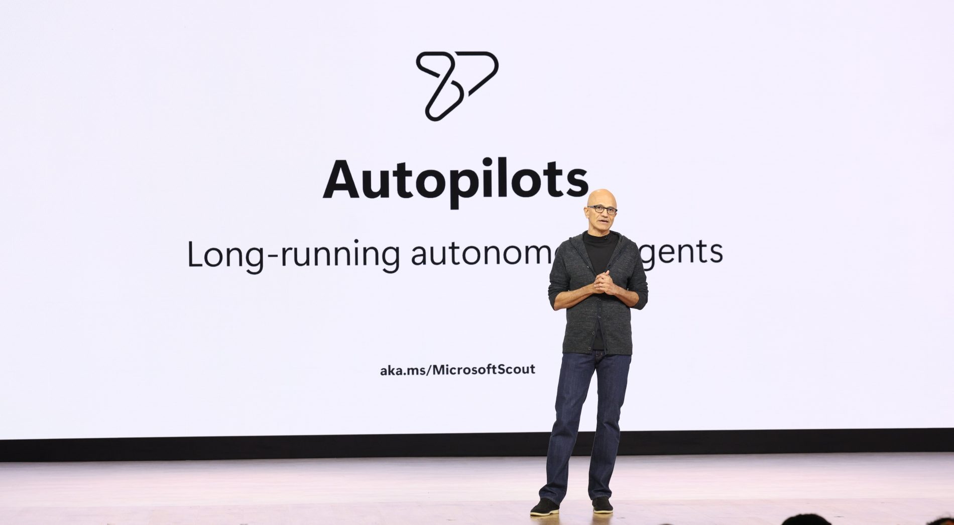 Satya Nadella onstage beside an Autopilots presentation describing long-running autonomous agents