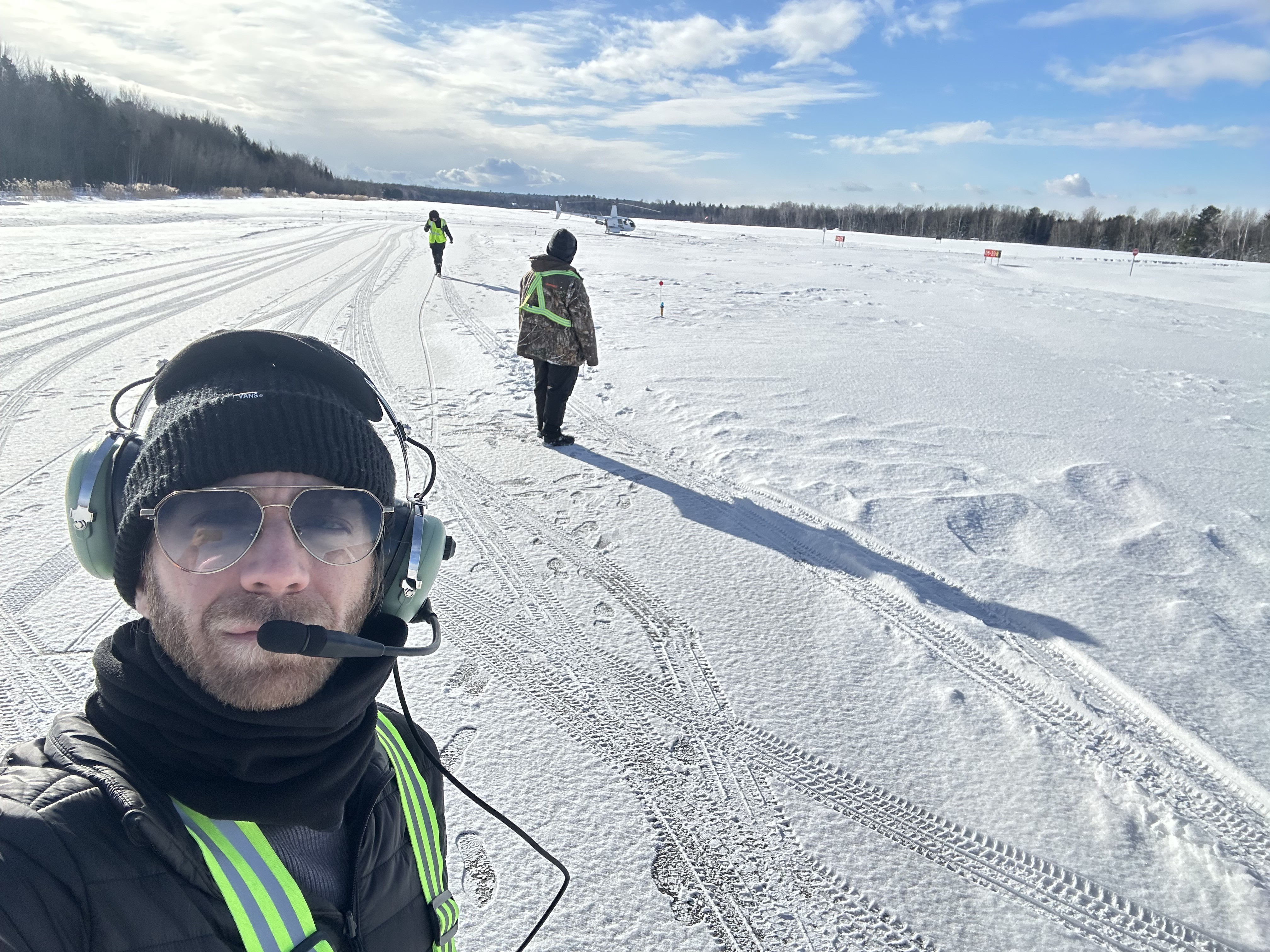 Mikaël Cardinal wearing a headset at a snow-covered flight-test site, with a helicopter in the distance