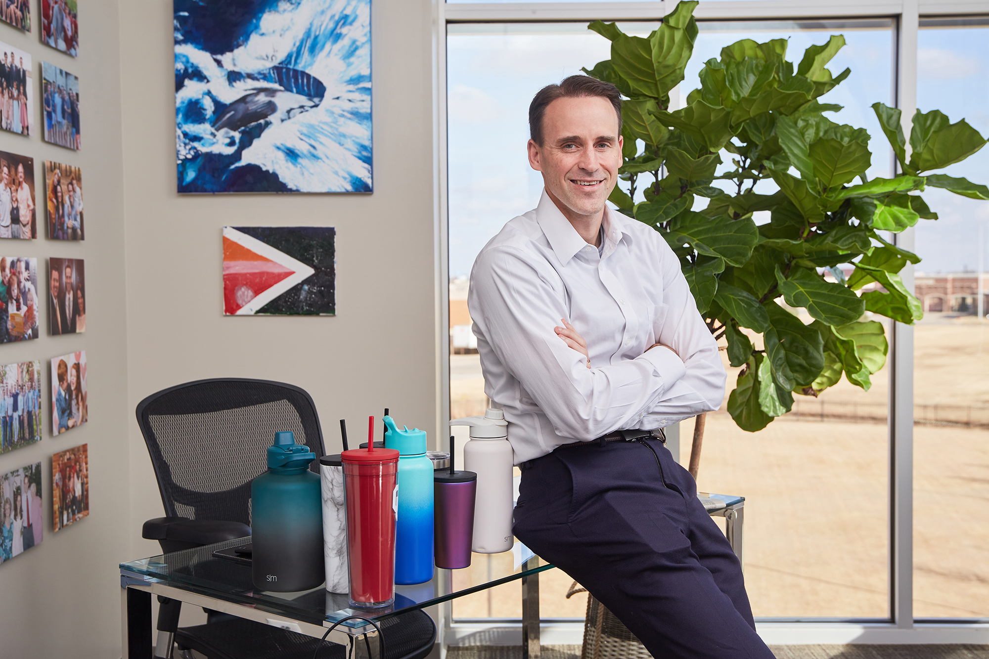 Mike Beckham in his office beside drinkware, a large plant and a wall of personal photographs
