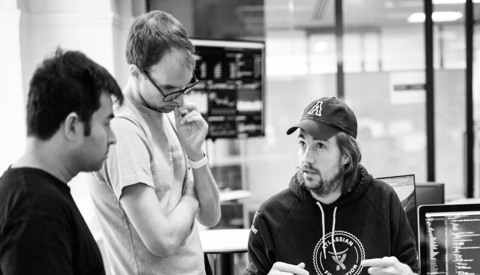 Mike Cannon-Brookes in an Atlassian cap and hoodie, discussing work with two colleagues