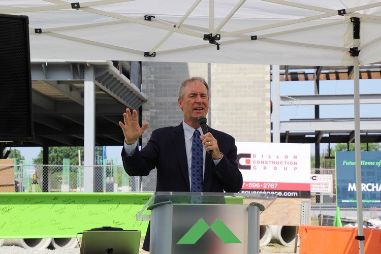 Mike Dunlap speaking under a canopy at the Merchants HQ2 topping-off ceremony, with construction visible behind him