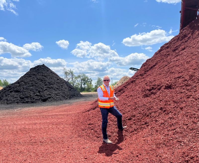 Mike Hachtman wearing a reflective vest beside large piles of recycled-pallet mulch at the McHenry plant