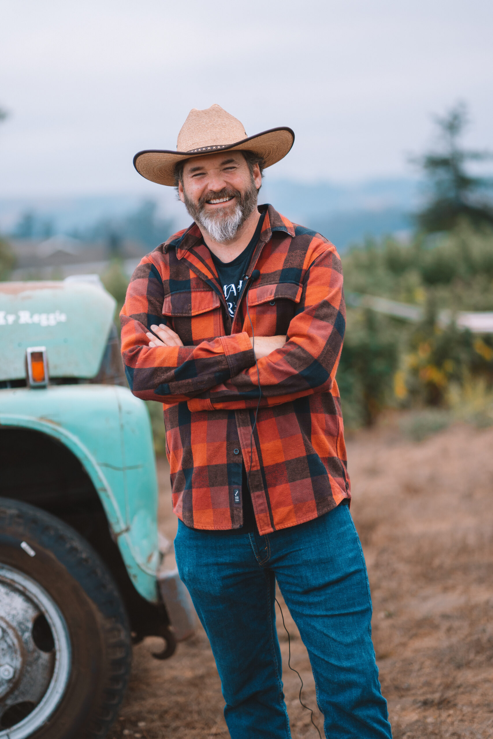 Mike Harden in a checked shirt and straw hat beside a vintage farm vehicle