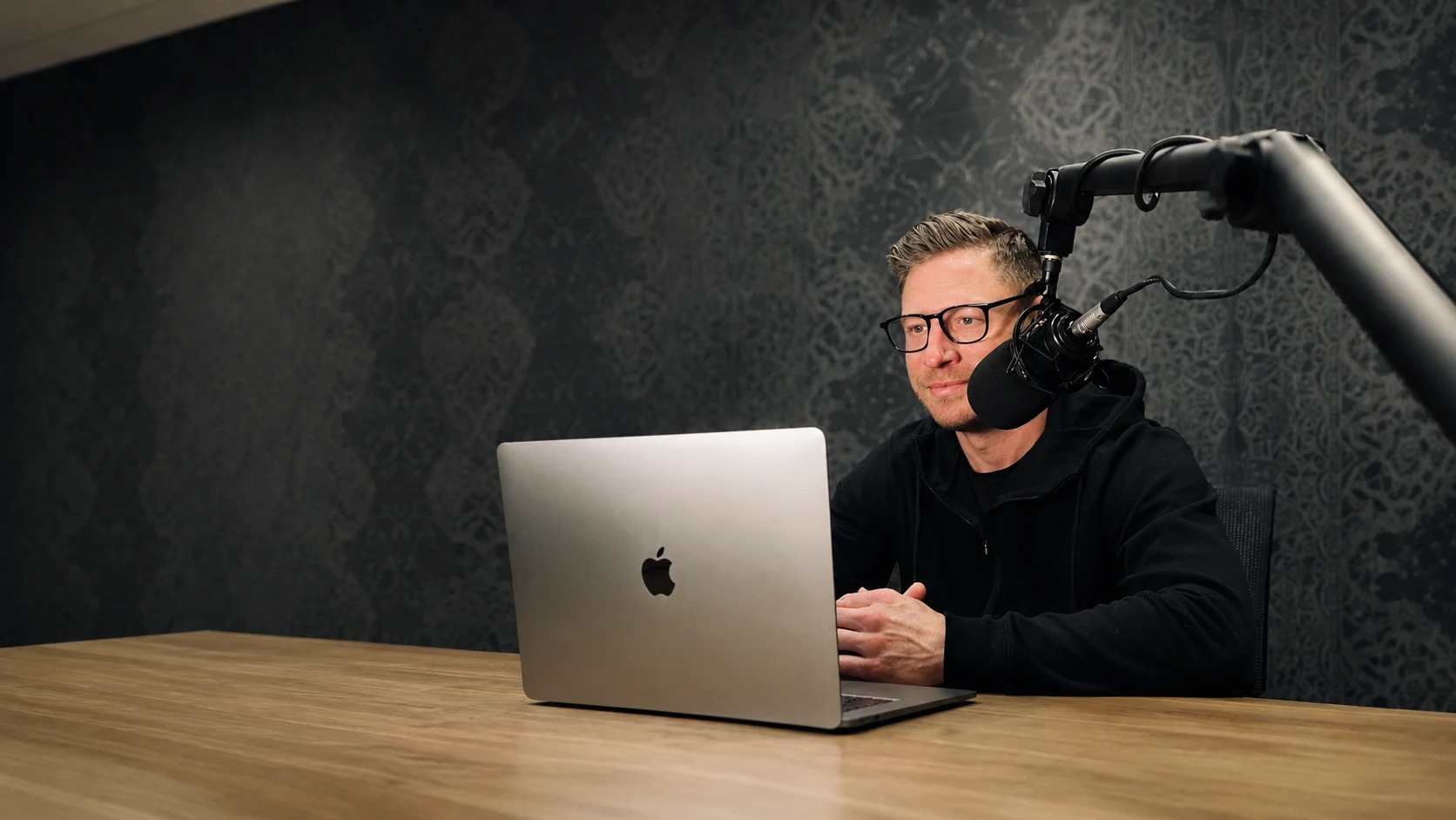 Mike Hardenbrook recording a podcast at a table with a studio microphone and laptop