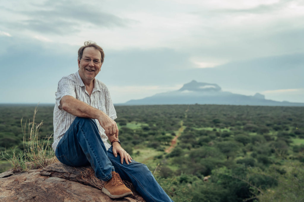 Mike Korchinsky sitting on a rock above a wooded landscape