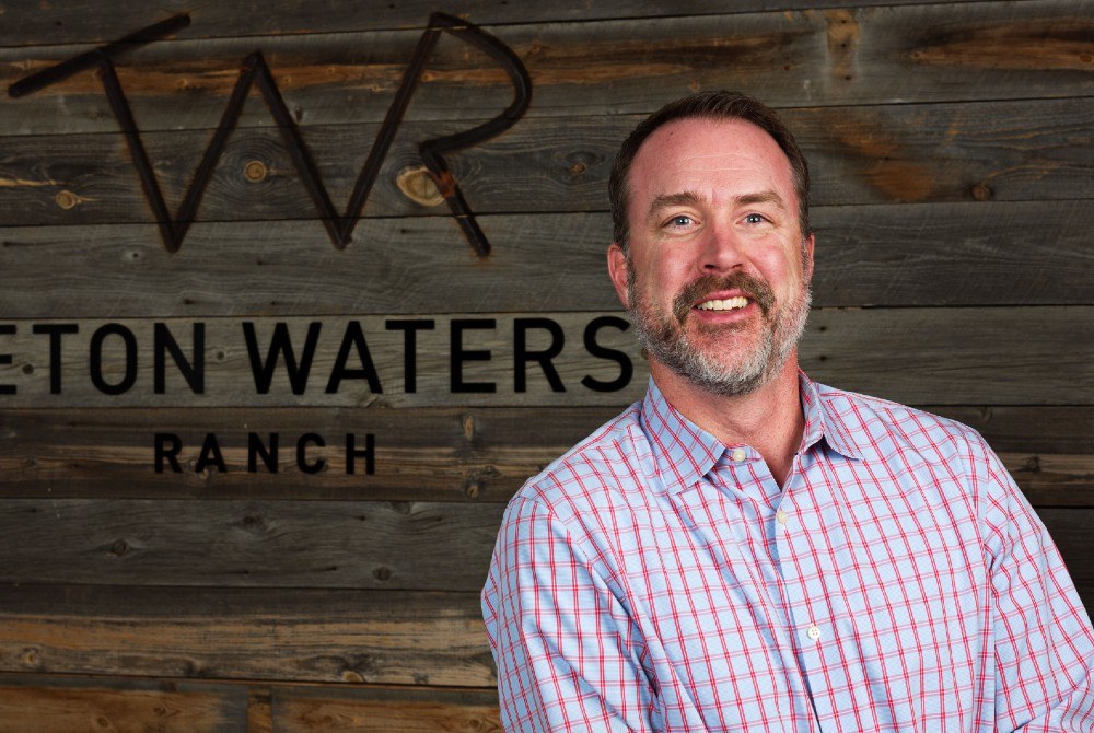 Mike Murray smiling in front of a wooden Teton Waters Ranch sign
