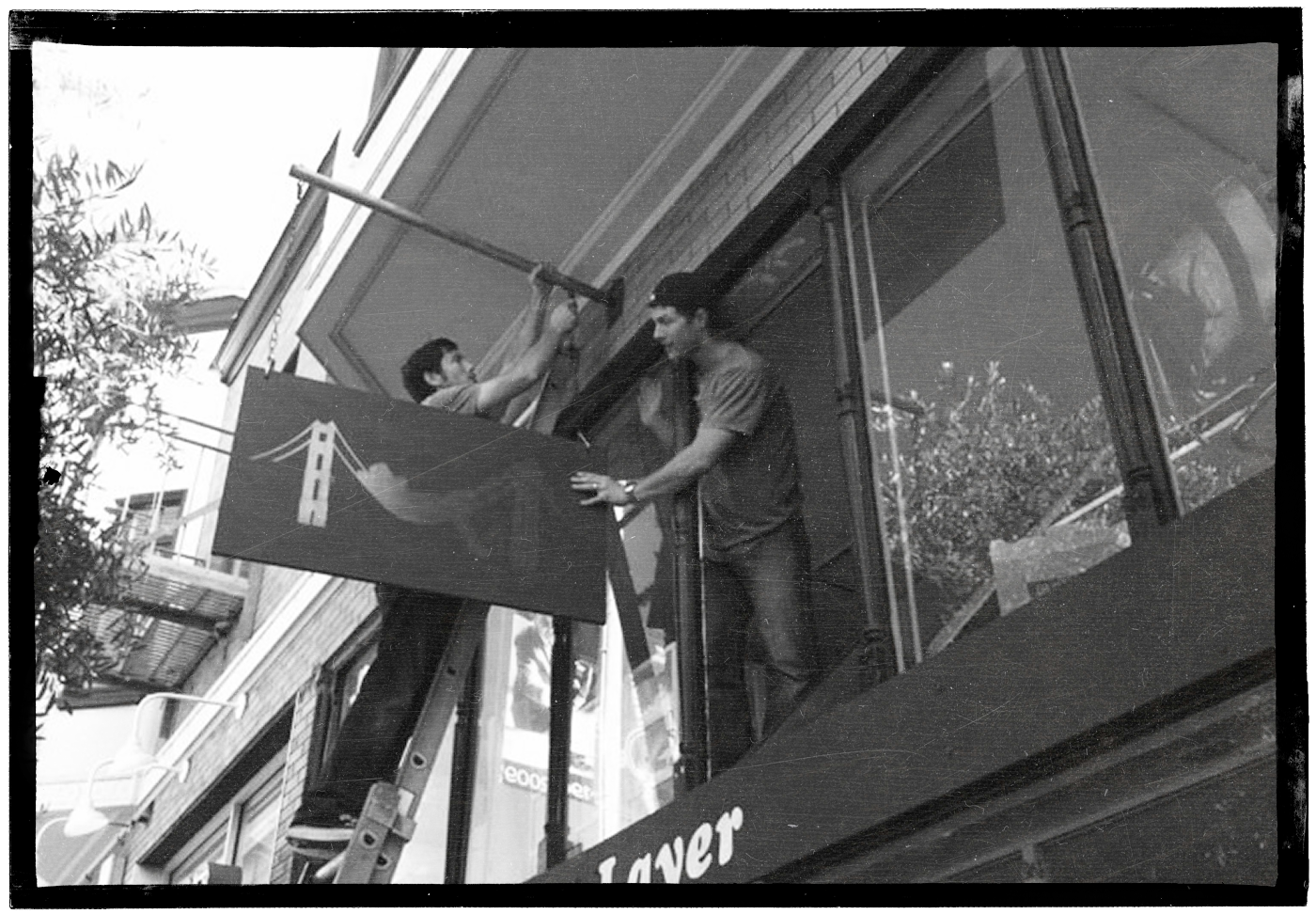 Marine Layer founders installing a sign above their San Francisco storefront
