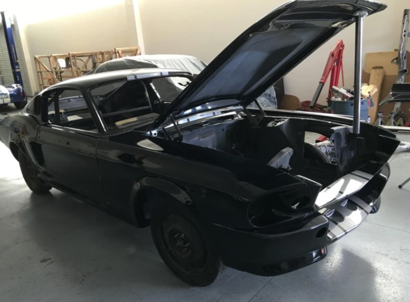 A black car under restoration, with its hood open in a workshop