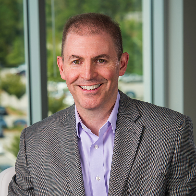 Mike Shapaker seated in an office, wearing a checked jacket and light purple shirt