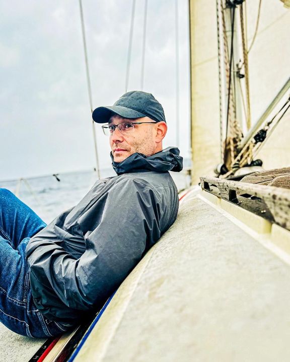 Mike Weiland in a cap and glasses, seated aboard a boat beside its rigging