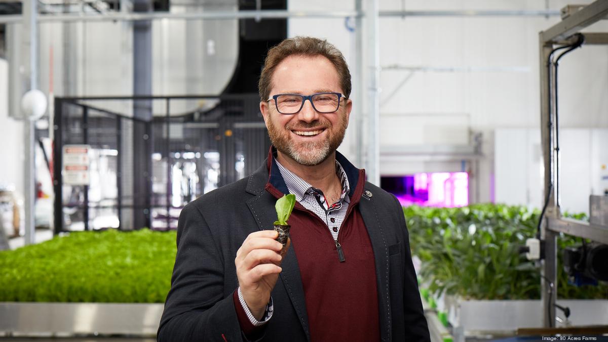 Mike Zelkind holds a young seedling inside an indoor farm, with rows of greens behind him