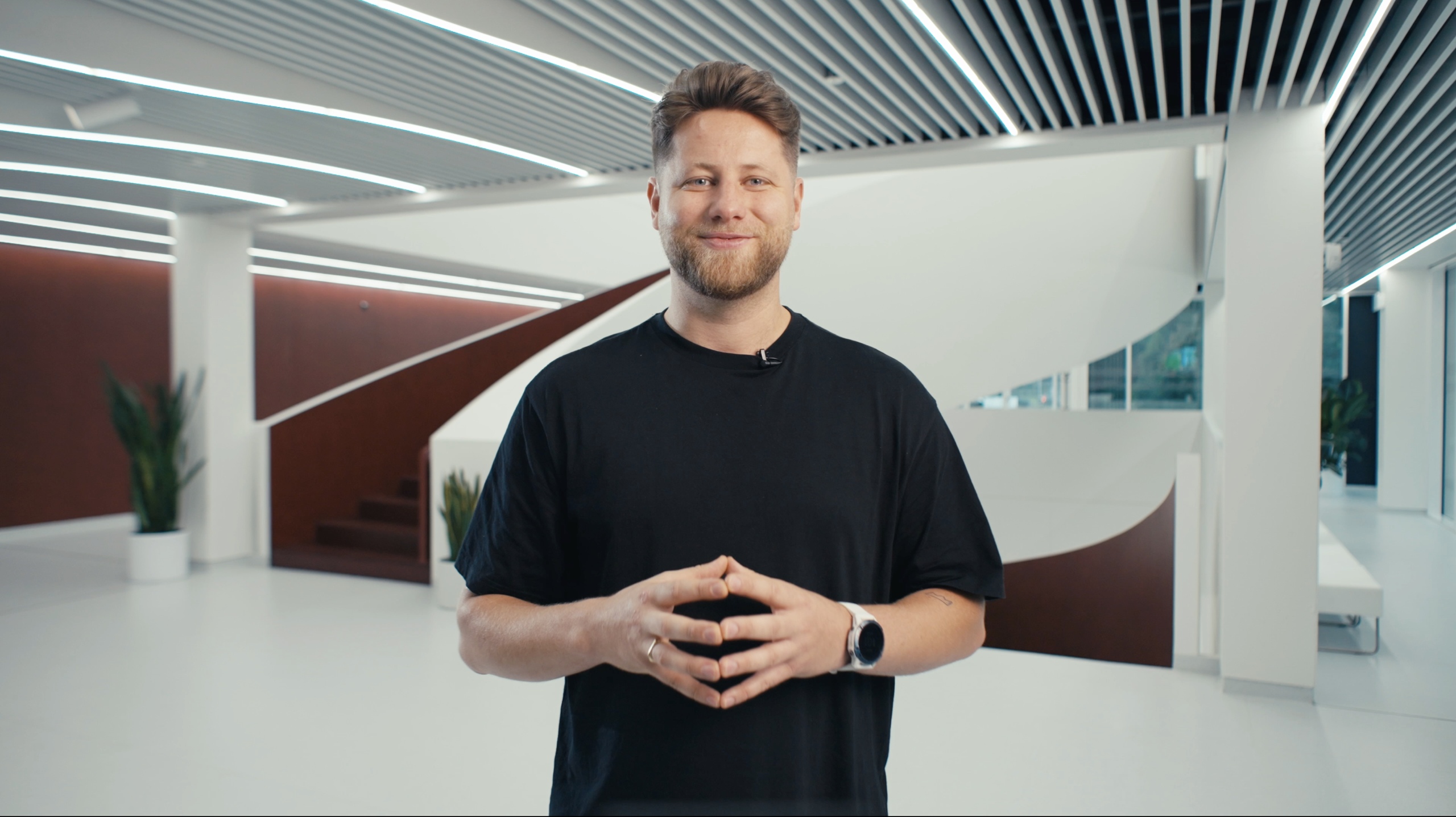 Mikus Opelts speaking in a bright interior with a curved staircase